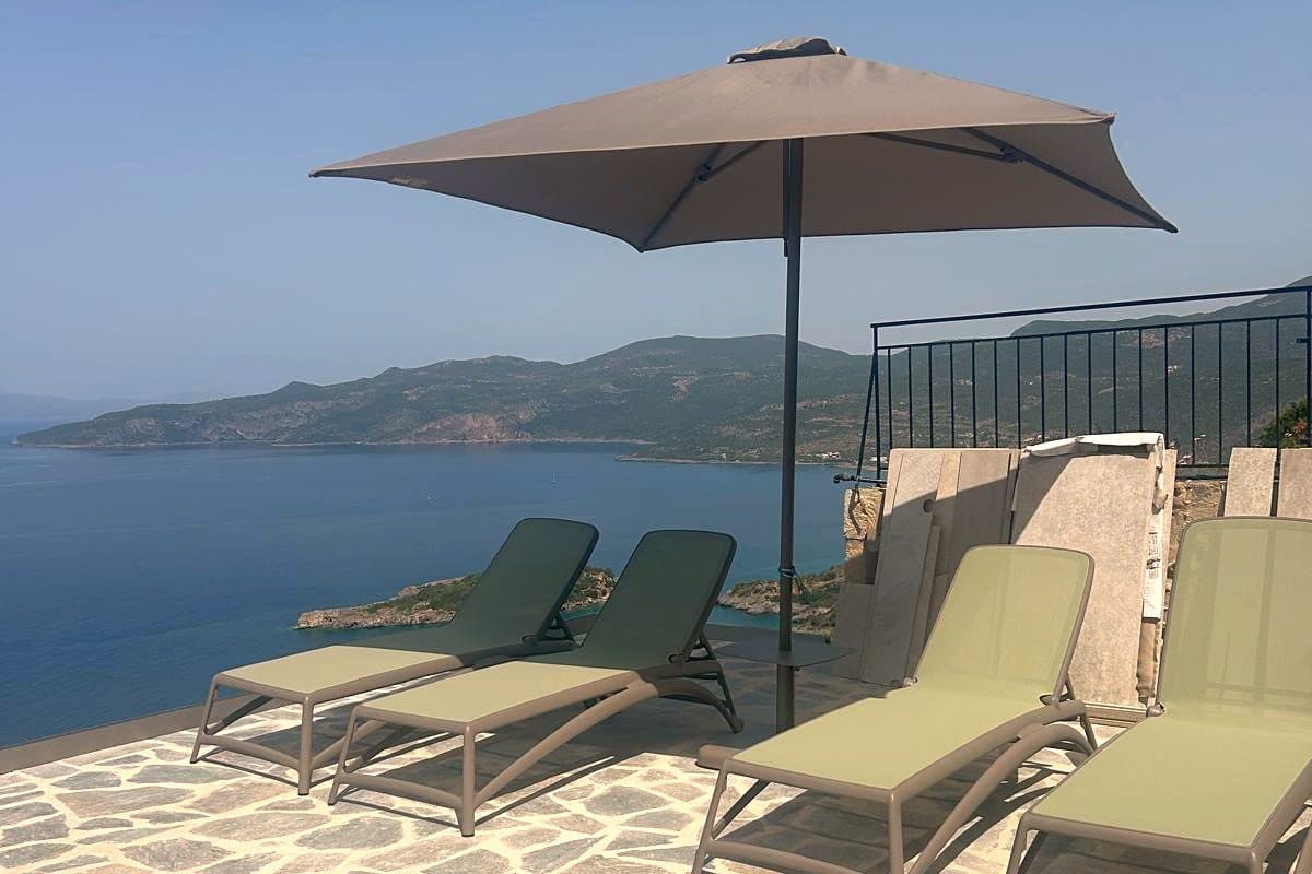 Sun loungers and a parasol on the stone terrace beside the pool.