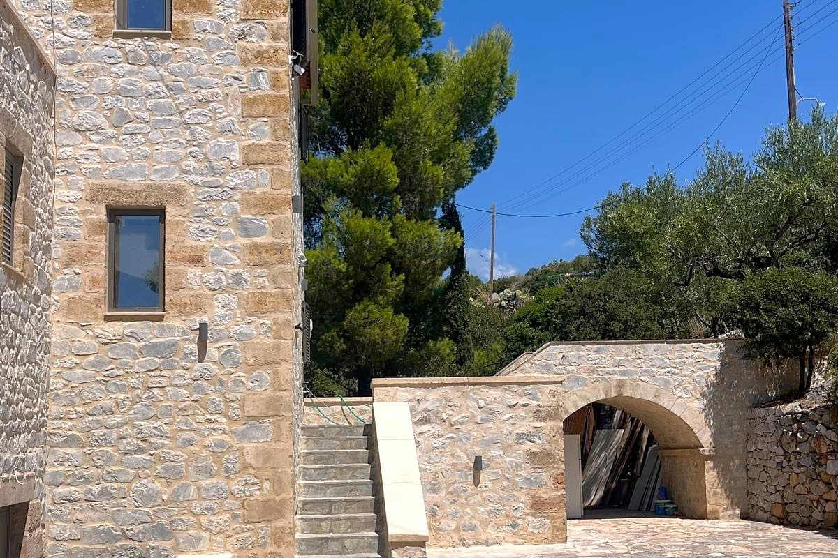 The stone exterior of the house, built in local limestone, with olive and cypress behind it.