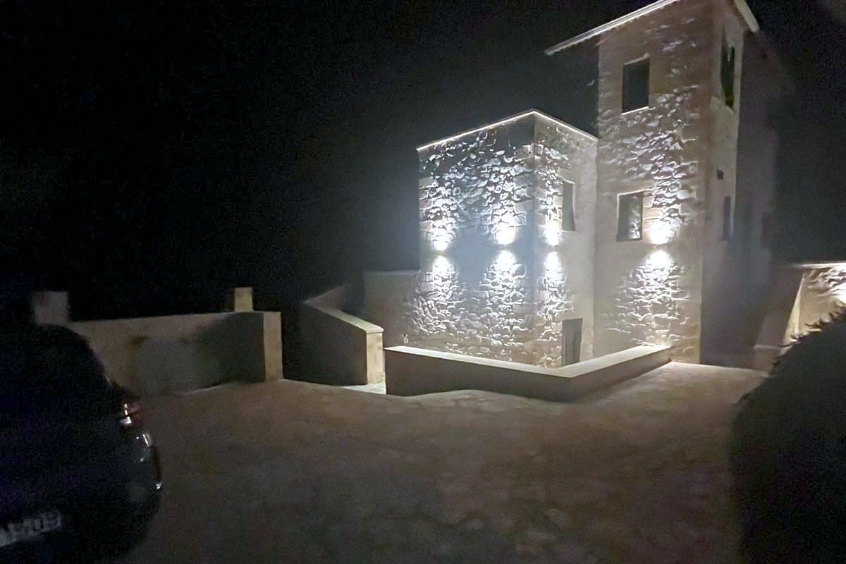 The house and terrace lit at night, with the pool in the foreground.