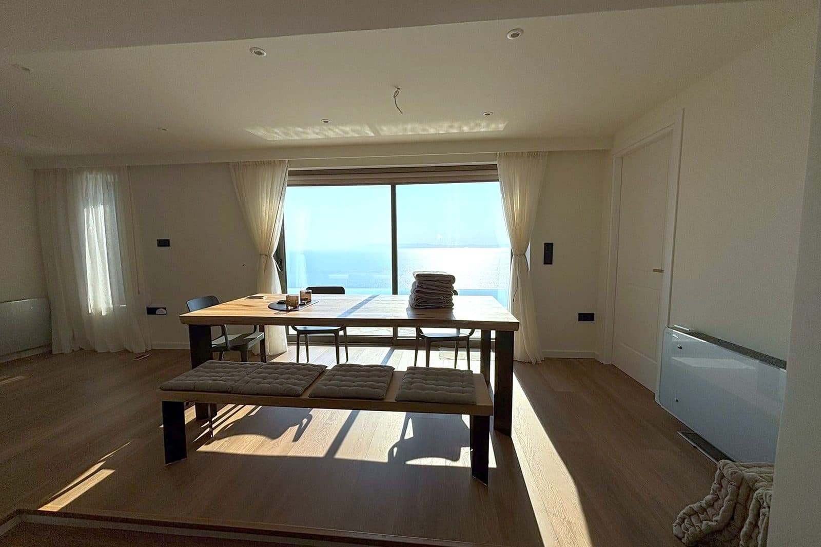 The dining table set in front of a window looking out to sea.